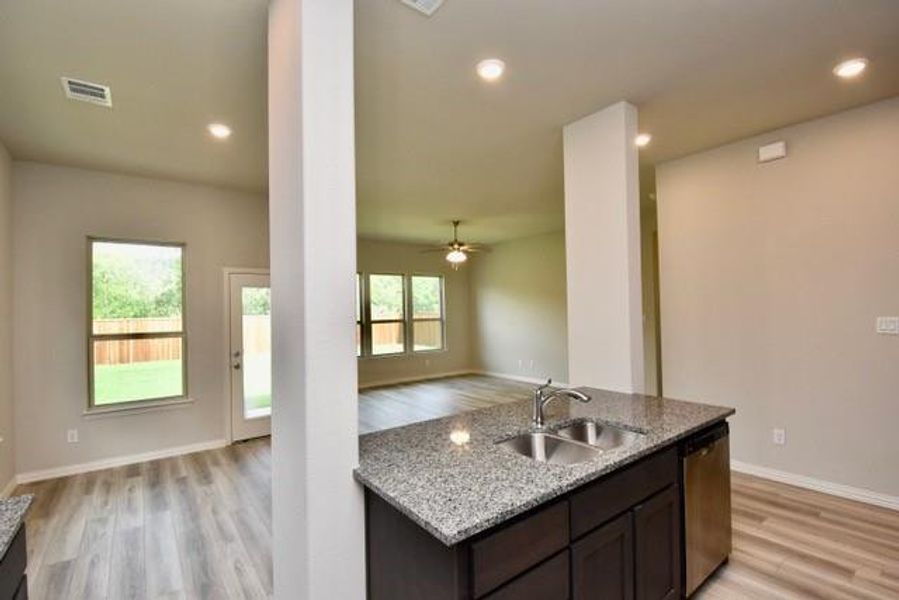 Kitchen with dishwasher, light wood-type flooring, granite counters, dark brown cabinets, and open floor plan Kitchen with dishwasher, light wood-type flooring, granite counters, dark brown cabinets, and open floor plan