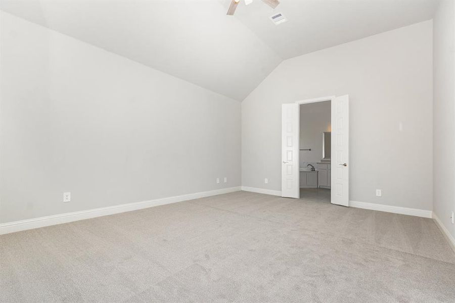 Unfurnished bedroom featuring light carpet, lofted ceiling, ensuite bath, and ceiling fan