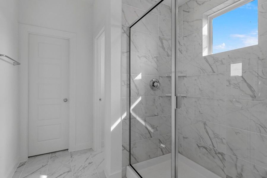 The primary bathroom features a spacious shower with a window above that brings in soft, natural light.