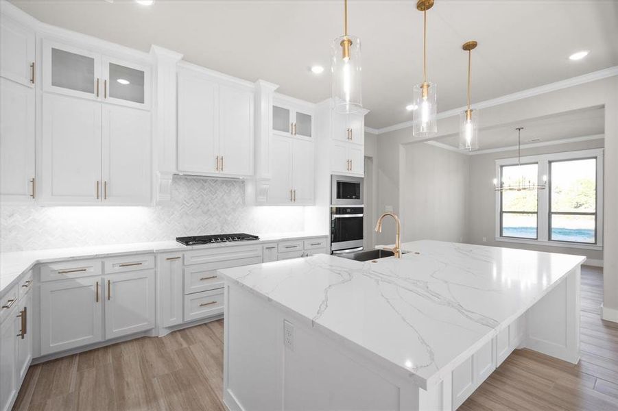 Kitchen featuring a center island with sink, hanging light fixtures, light hardwood / wood-style flooring, light stone counters, and white cabinetry