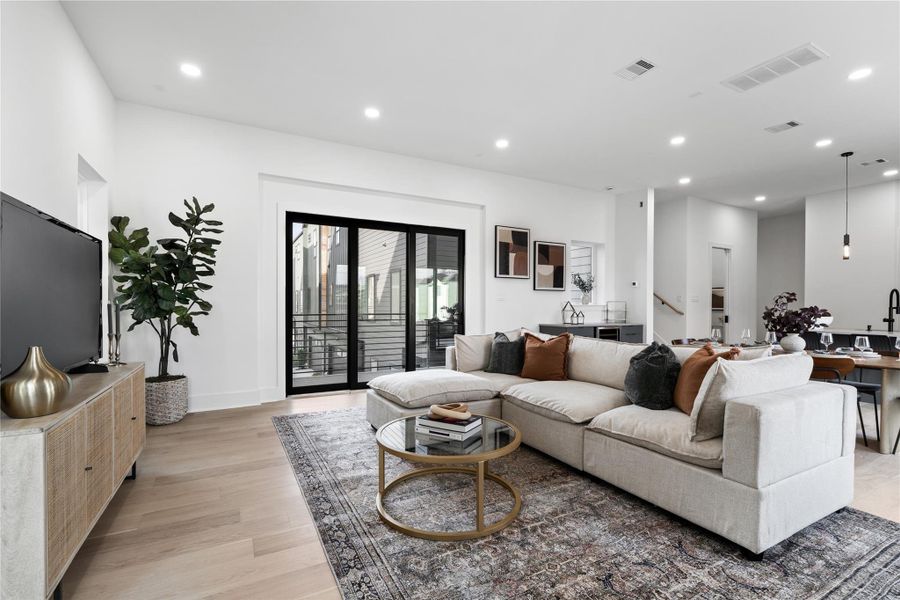 The living area is filled with natural light and warmth. Light wood floors and crisp white walls enhance the airy atmosphere, while recessed lighting adds a modern touch. The space flows seamlessly into the adjacent areas, offering an ideal layout for both relaxation and entertaining.