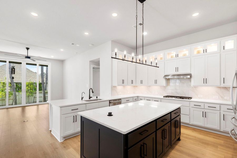 Sunlit open kitchen with oversized quartz island, sleek pendant lighting, and wide sliding doors to backyard.