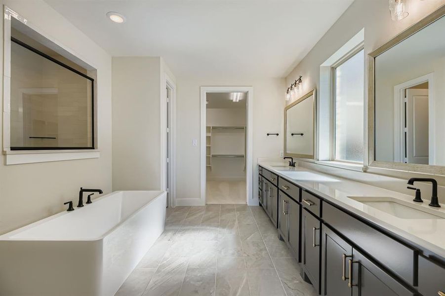 Full bathroom featuring a freestanding bath, double vanity, a walk in closet, recessed lighting, and light marble finish flooring