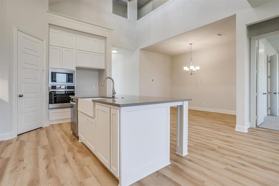 Kitchen with white cabinetry, light hardwood / wood-style flooring, appliances with stainless steel finishes, and a center island with sink