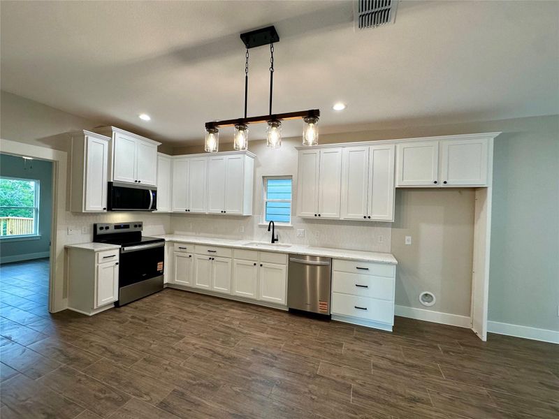 Kitchen with appliances with stainless steel finishes, dark wood-type flooring, white cabinetry, light countertops, and recessed lighting Kitchen with appliances with stainless steel finishes, dark wood-type flooring, white cabinetry, light countertops, and recessed lighting