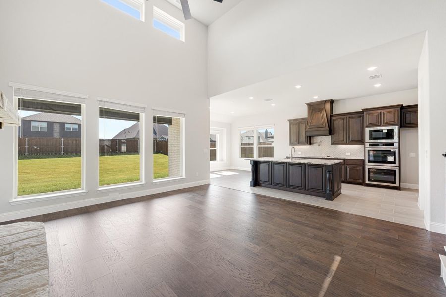 Open living area with soaring ceilings and hardwood floors flowing into kitchen with dark cabinets and island Open living area with soaring ceilings and hardwood floors flowing into kitchen with dark cabinets and island