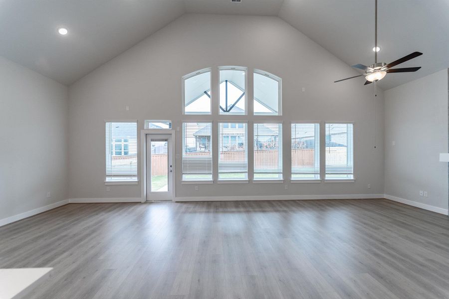 Unfurnished living room with ceiling fan, healthy amount of natural light, a high ceiling, and light wood-type flooring