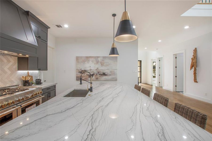 Kitchen with light stone countertops, sink, tasteful backsplash, range with two ovens, and decorative light fixtures