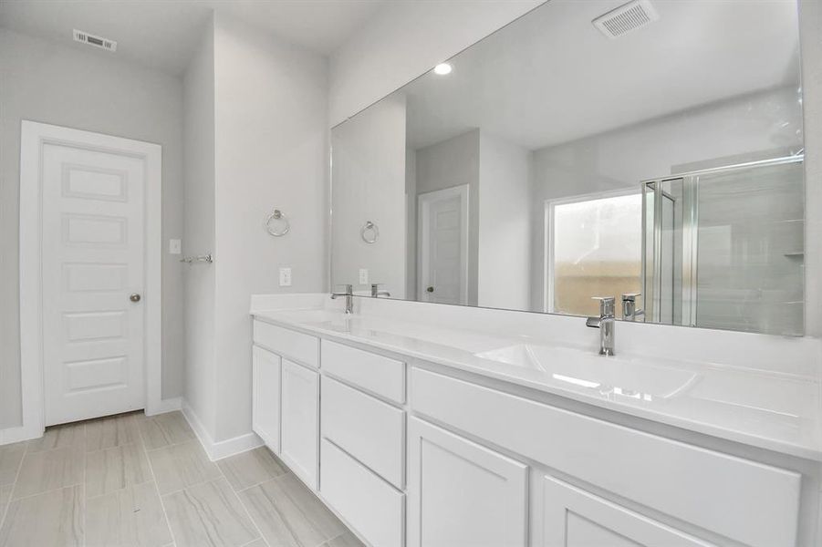 Experience luxury in this spa-like primary bathroom featuring a massive walk-in shower with tile surround. Light colored cabinets with light granite countertops complement the space, alongside a spacious walk-in closet with shelving, high ceilings, custom paint, and sleek, dark modern finishes.