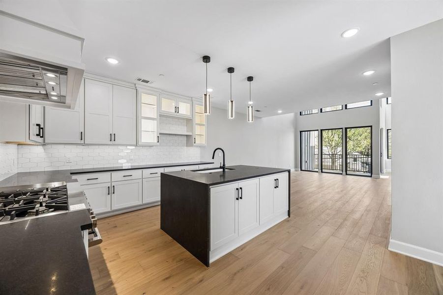 Kitchen with a kitchen island with sink, white cabinetry, stainless steel range with gas cooktop, light wood-type flooring, and open floor plan Kitchen with a kitchen island with sink, white cabinetry, stainless steel range with gas cooktop, light wood-type flooring, and open floor plan