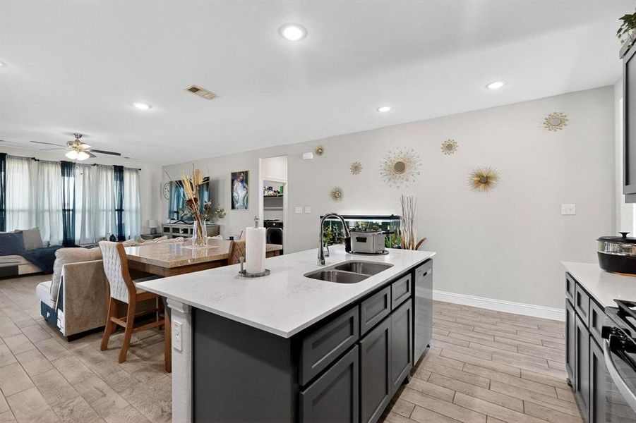 Kitchen featuring open floor plan, wood tiled floors, light stone counters, an island with sink, and recessed lighting Kitchen featuring open floor plan, wood tiled floors, light stone counters, an island with sink, and recessed lighting