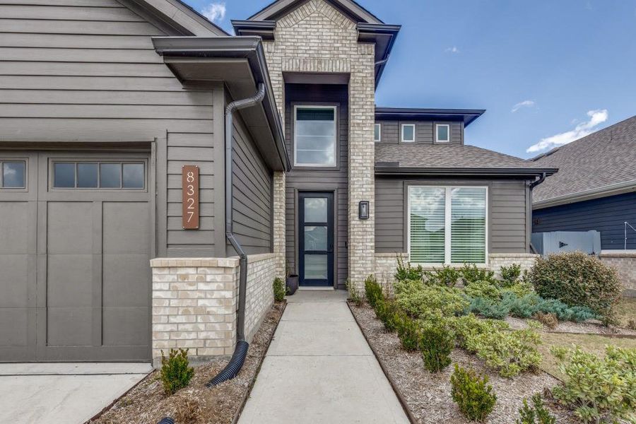 Modern home with a sleek exterior featuring dark siding and brick accents. It has a prominent entrance, large windows, and well-maintained landscaping. The house number is clearly displayed