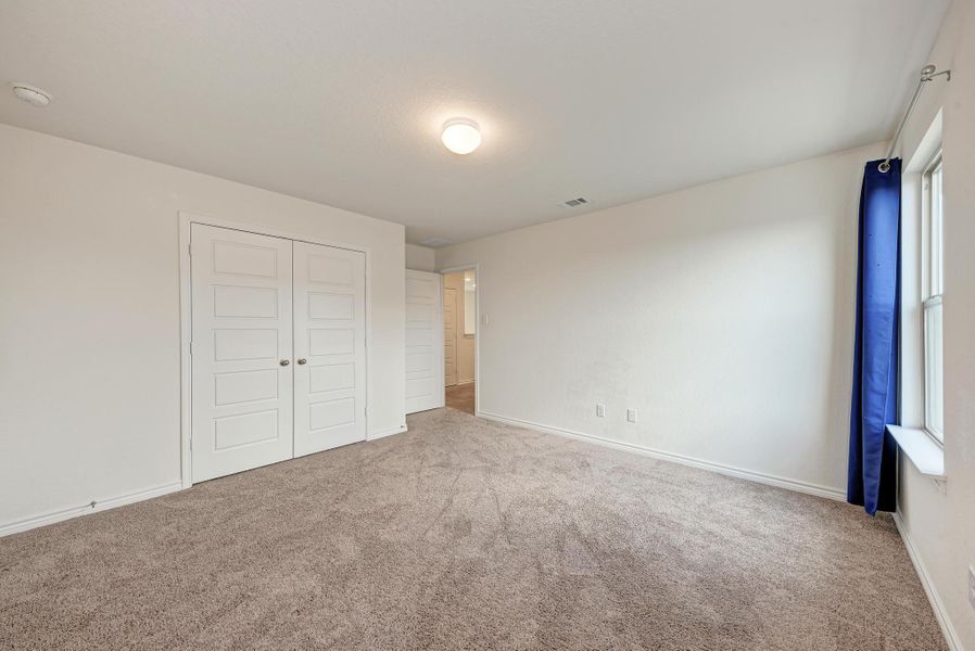 A well-lit bedroom features ample floor space, soft carpet, and a pair of white bifold doors.