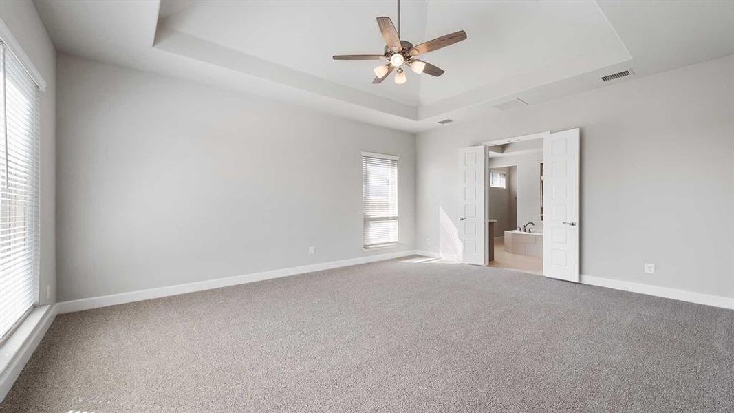 Carpeted empty room featuring ceiling fan and a raised ceiling