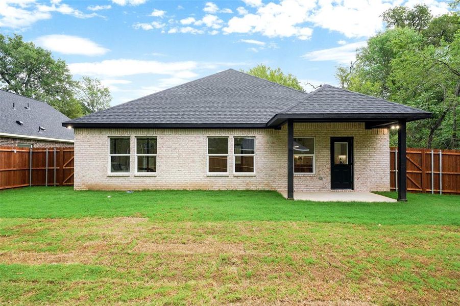 Rear exterior featuring light-colored brick siding, a dark shingle roof, a covered patio with dark support beams, and a dark exterior door Rear exterior featuring light-colored brick siding, a dark shingle roof, a covered patio with dark support beams, and a dark exterior door