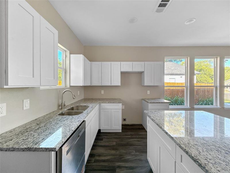 Kitchen with white cabinetry, light stone countertops, and dishwasher