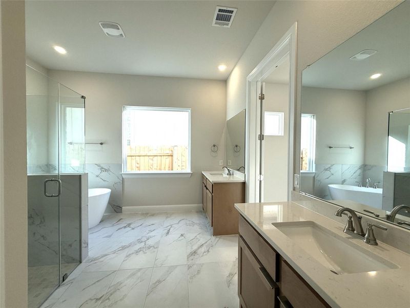 Full bath with a freestanding bath, a marble finish shower, light marble finish flooring, two vanities, and recessed lighting