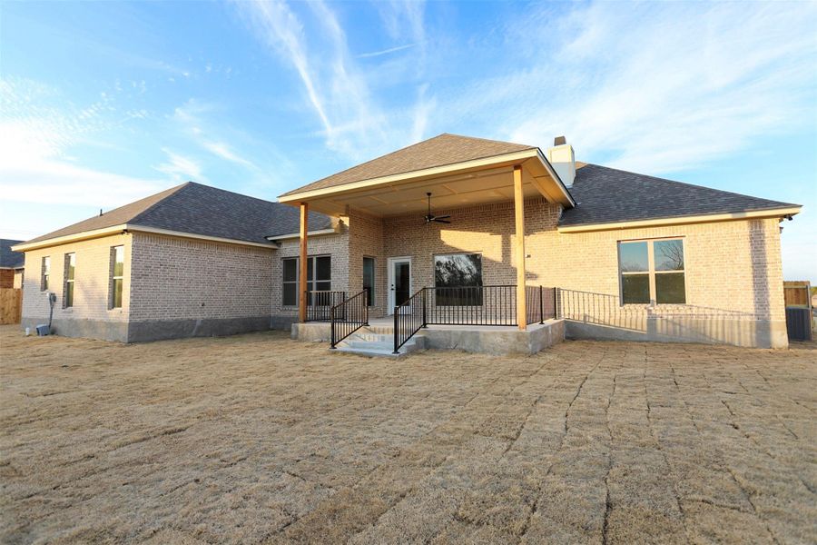 Back of property with ceiling fan, a chimney, a patio, brick siding, and a shingled roof