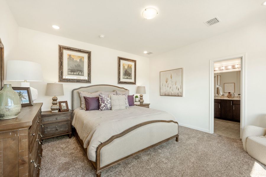 Master bedroom with upholstered bed, wood dresser, carpet flooring, and ensuite bathroom visible through doorway