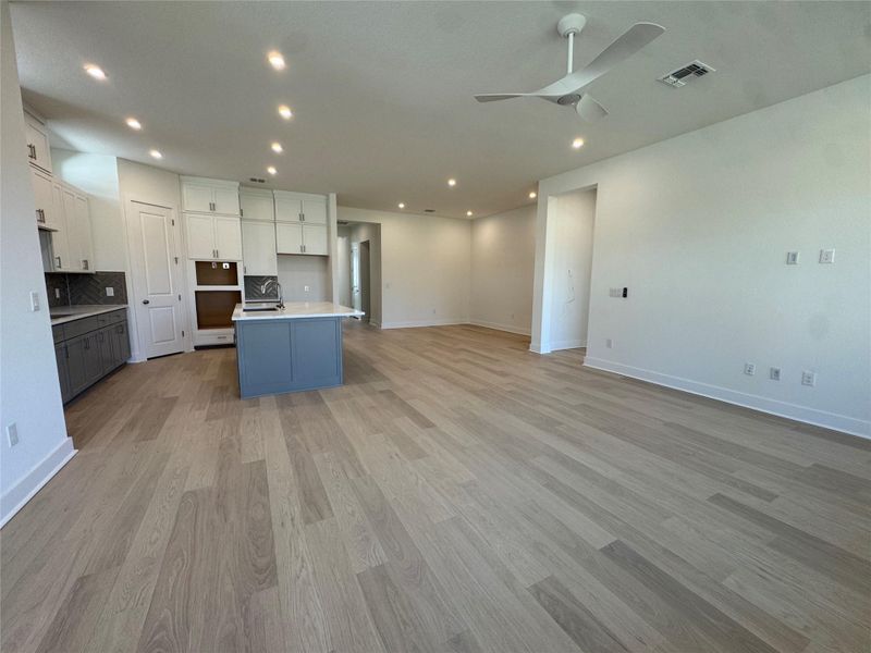Kitchen featuring open floor plan, a kitchen island with sink, two tone color scheme, a ceiling fan, and backsplash