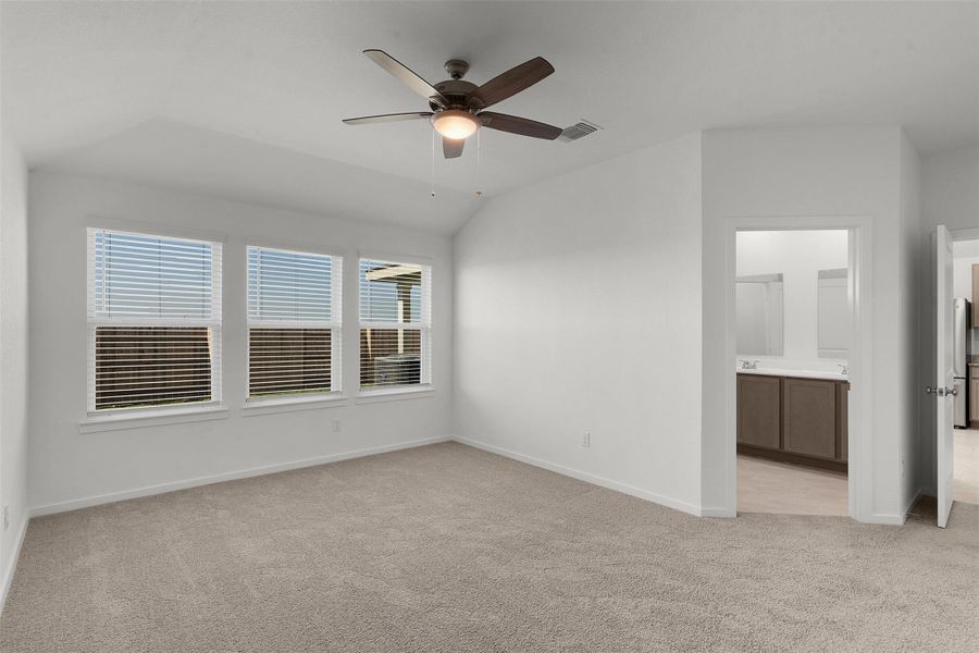 Unfurnished bedroom featuring light colored carpet, a ceiling fan, vaulted ceiling, ensuite bathroom, and freestanding refrigerator