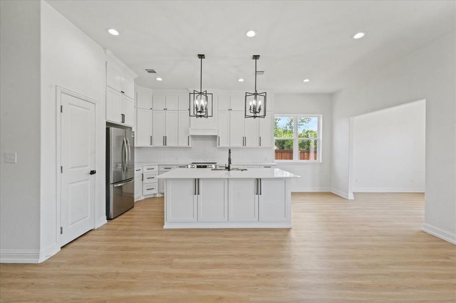 Modern kitchen featuring white cabinetry, a center island with pendant lighting, stainless steel appliances, and wood-finish flooring