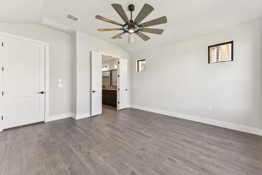 Unfurnished bedroom with lofted ceiling, ensuite bathroom, light wood-type flooring, and a ceiling fan Unfurnished bedroom with lofted ceiling, ensuite bathroom, light wood-type flooring, and a ceiling fan