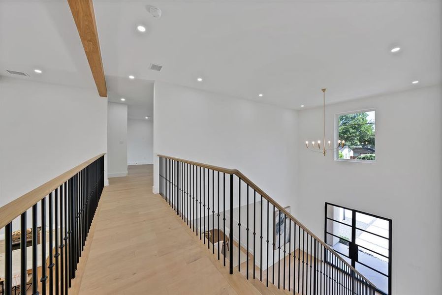 Upper level hallway with wood-finish flooring and black wrought iron balusters