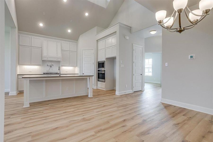 Kitchen featuring white cabinets, stainless steel appliances, hanging light fixtures, and light wood-type flooring