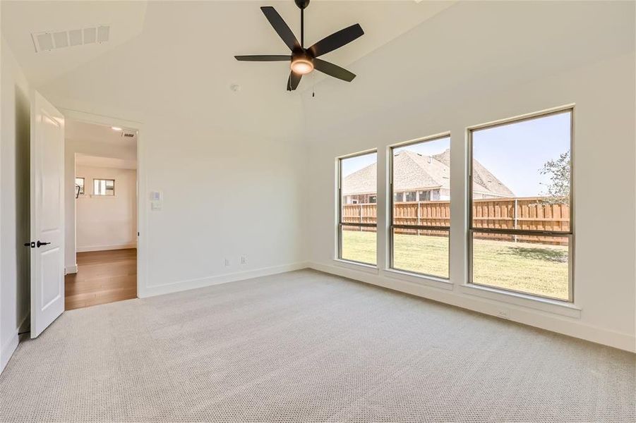 Carpeted empty room with high vaulted ceiling and ceiling fan