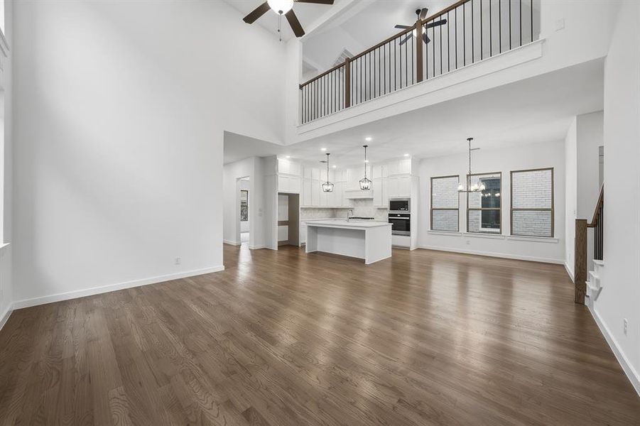Unfurnished living room featuring dark wood finished floors, a chandelier, a ceiling fan, and a towering ceiling