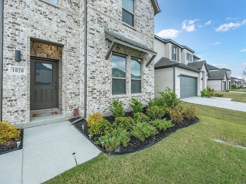 View of exterior entry with brick siding, driveway, a lawn, and a garage