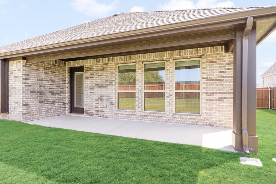 Covered back patio with concrete slab, brick exterior, and fenced backyard with green lawn