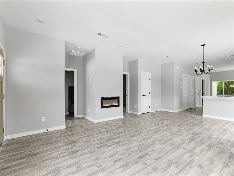 Unfurnished living room with light wood-style floors, a chandelier, a glass covered fireplace, and baseboards
