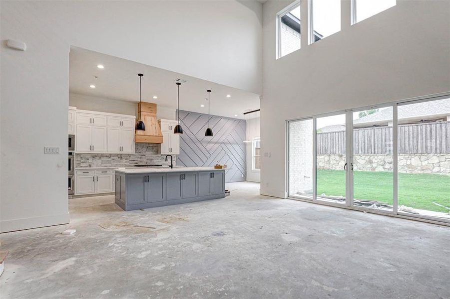 Kitchen featuring premium range hood, a towering ceiling, an island with sink, decorative light fixtures, and white cabinetry