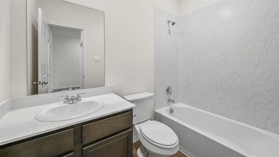 Bathroom featuring a white drop-in sink with chrome faucet, dark wood-finish vanity, light-colored countertop, and a white tub with integrated shower