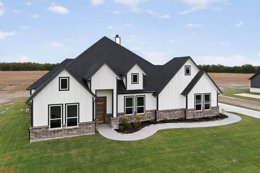View of front of property featuring board and batten siding, a front lawn, roof with shingles, and brick siding View of front of property featuring board and batten siding, a front lawn, roof with shingles, and brick siding