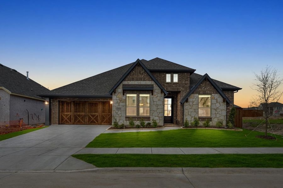Single-story home with brick and stone exterior, wood garage doors, and green lawn at dusk