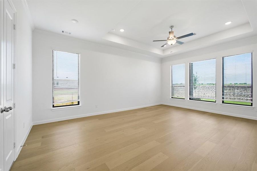 Spacious room featuring light wood-finish flooring, a tray ceiling with a contemporary ceiling fan, and recessed lighting Spacious room featuring light wood-finish flooring, a tray ceiling with a contemporary ceiling fan, and recessed lighting