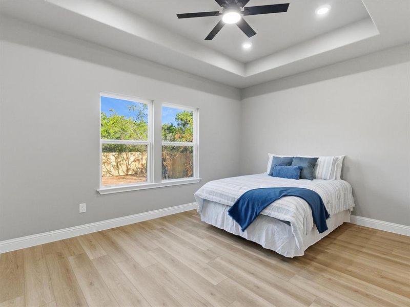 Bedroom with a raised ceiling, light wood-type flooring, ceiling fan, and recessed lighting Bedroom with a raised ceiling, light wood-type flooring, ceiling fan, and recessed lighting