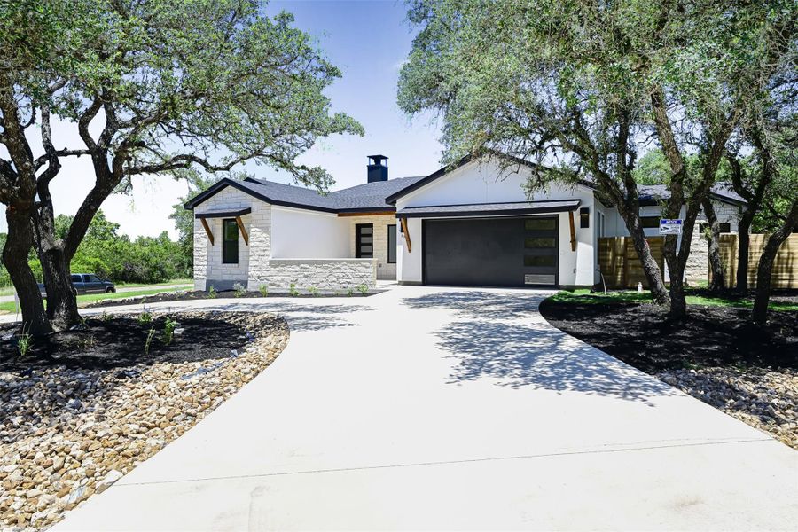 View of front of property with curved driveway, stone siding, a chimney, an attached garage, and stucco siding