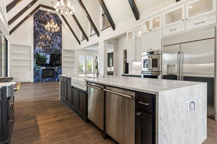 Kitchen featuring light stone counters, appliances with stainless steel finishes, dark cabinetry, a spacious island, and high vaulted ceiling Kitchen featuring light stone counters, appliances with stainless steel finishes, dark cabinetry, a spacious island, and high vaulted ceiling