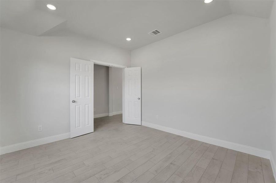 Unfurnished bedroom featuring light wood finished floors, baseboards, visible vents, and vaulted ceiling