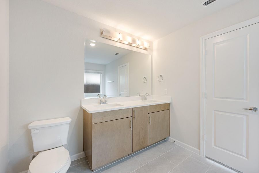 Bathroom with double-sink vanity, wood cabinets, large mirror with light bar, and tile floors