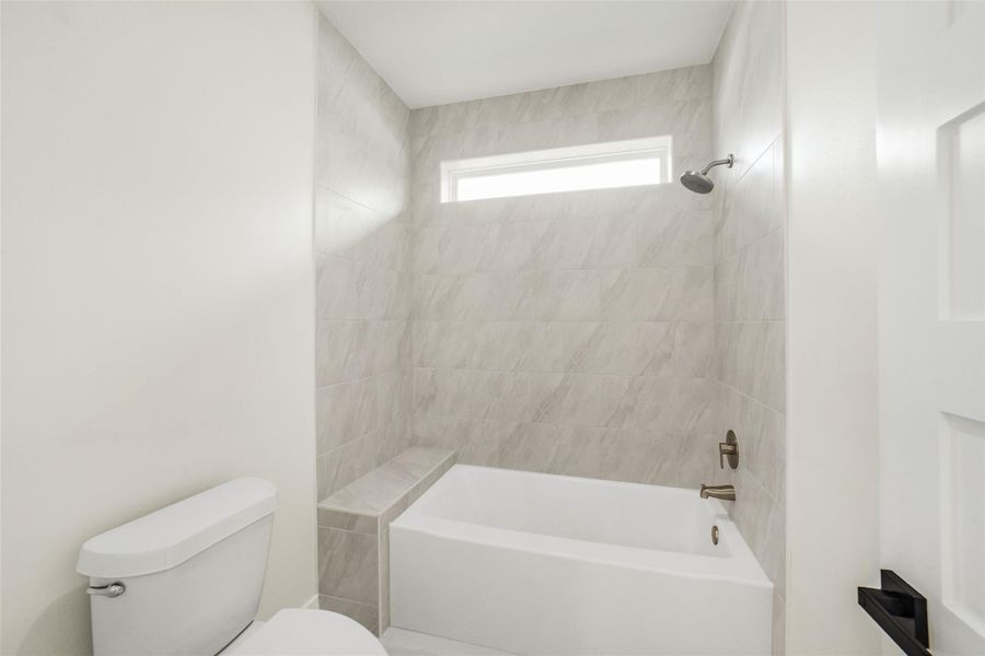 Modern bathroom with a sleek tub-shower combo, light gray tile surround, and a narrow horizontal window for natural light.