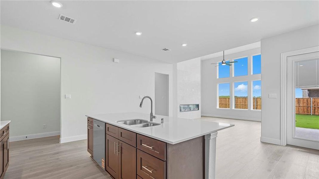 Kitchen island featuring a stainless steel sink with a gooseneck faucet, integrated dishwasher, and rich wood cabinetry