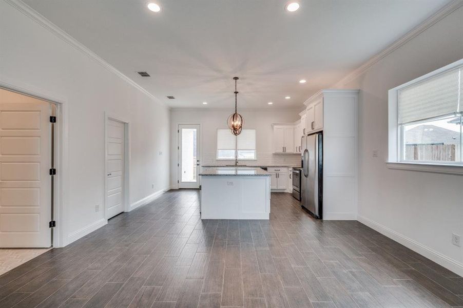 Kitchen with ornamental molding, stainless steel appliances, decorative light fixtures, white cabinetry, and a kitchen island