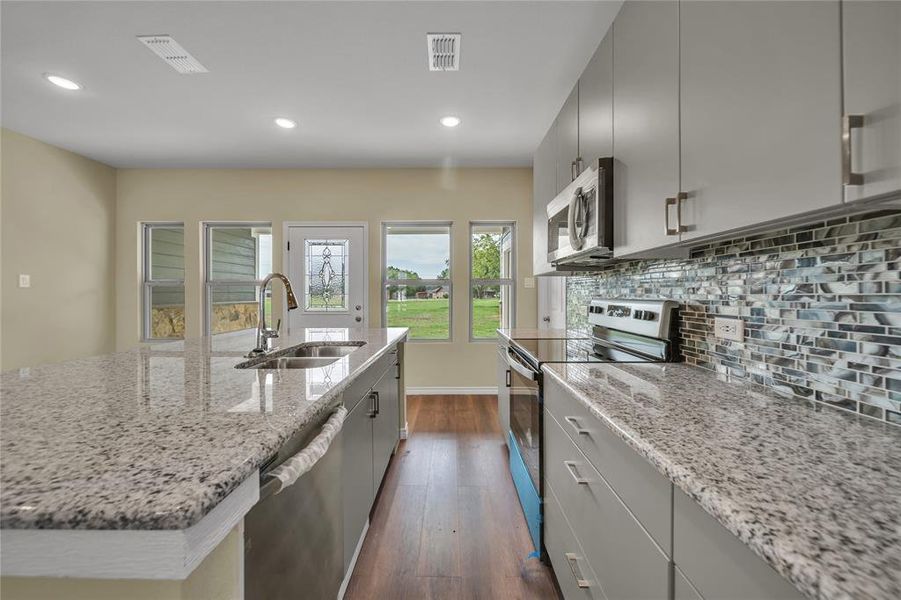 Kitchen featuring appliances with stainless steel finishes, tasteful backsplash, gray cabinetry, sink, and dark hardwood / wood-style flooring