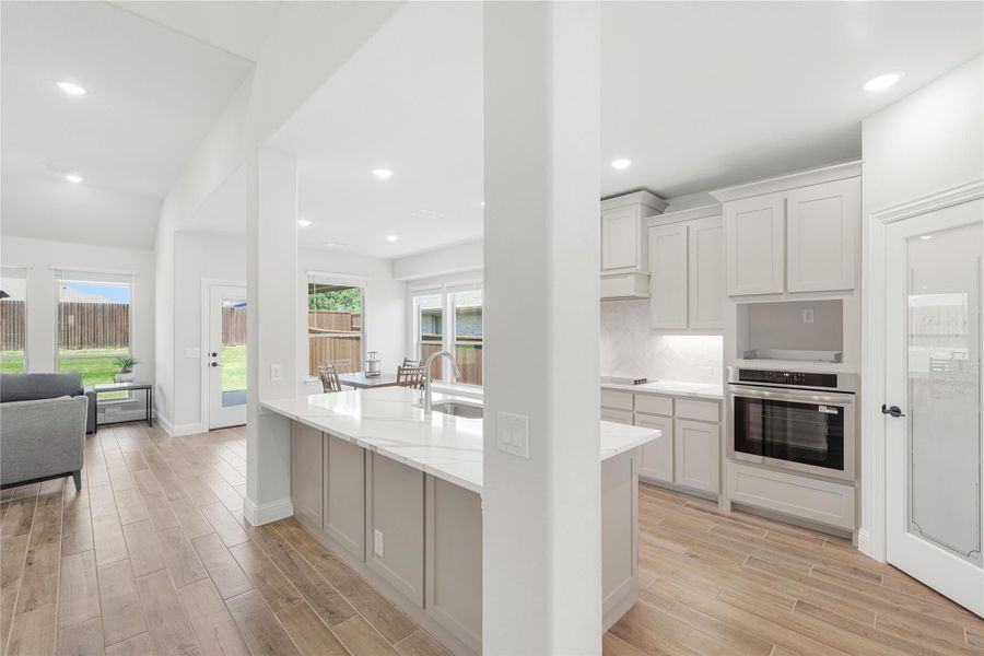 Open kitchen with gray cabinets, white quartz island, stainless steel oven, and wood-look tile floors Open kitchen with gray cabinets, white quartz island, stainless steel oven, and wood-look tile floors