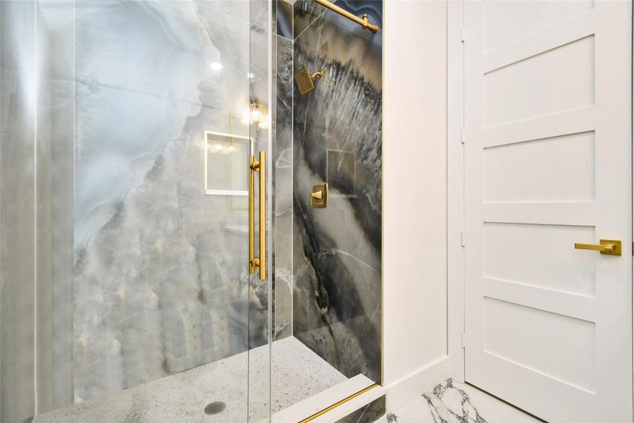 Sophisticated vanity area featuring a white quartz countertop, under-mount sink, and designer gold-toned faucet. Bold marble-patterned tile flooring and crystal vanity lighting complete this elegant and functional space.